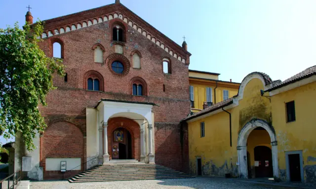 Morimondo cosa vedere: imponente facciata in mattoni rossi di un'antica abbazia, con scalinata e portico. Accanto, un edificio giallo con un arco.
