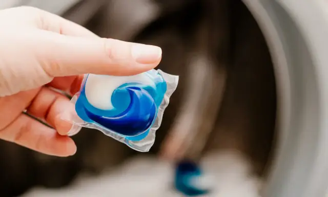 Mano sostiene una cápsula de detergente azul y blanca lista para usar en la lavadora.
