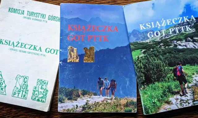 Trzy książeczki GOT PTTK z odznakami. Jedna biała z zielonymi symbolami, dwie z górskimi krajobrazami.