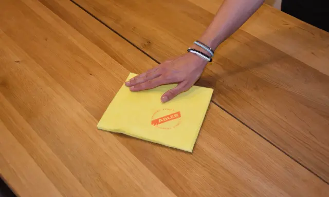 Hand wischt mit gelbem Tuch über Holzoberfläche, um den holztisch aufhellen.