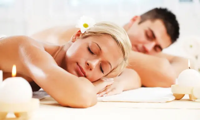 Para relaksująca się w SPA, z kwiatkiem we włosach, obok płonących świec.