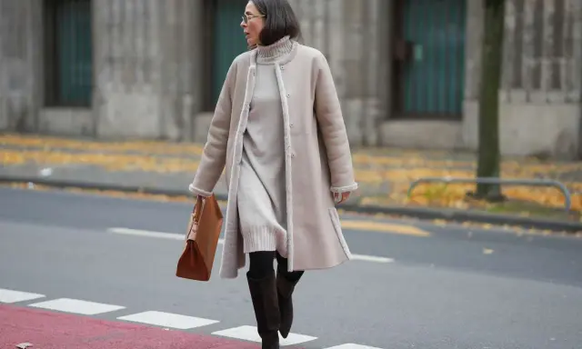 A woman demonstrates how to layer a dress for winter with a cozy turtleneck dress, a shearling coat, and stylish boots.