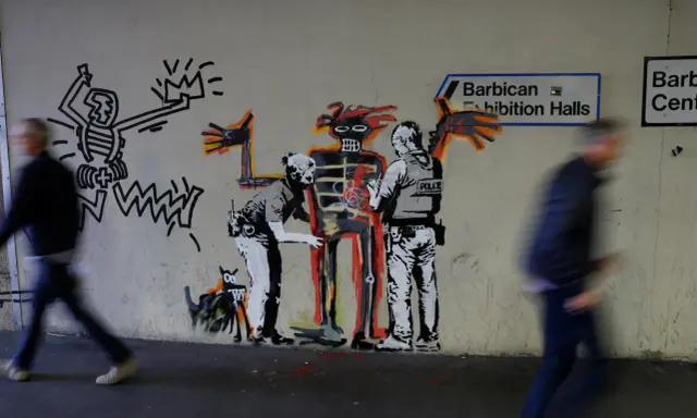 Famous graffiti depicts two police officers interacting with a skeletal figure, with a Keith Haring-esque character and a dog nearby.