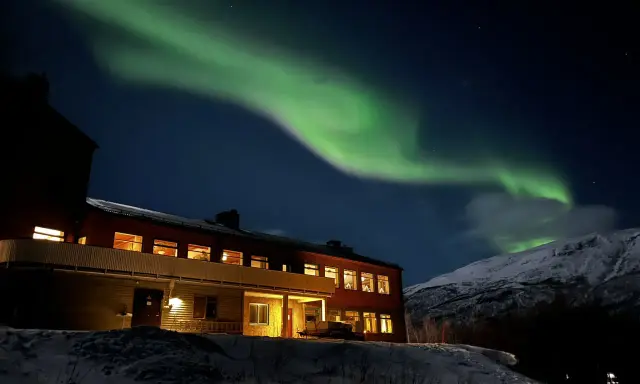 Norrsken över ett snötäckt landskap med ett hus. Perfekt för kiruna sightseeing turer.