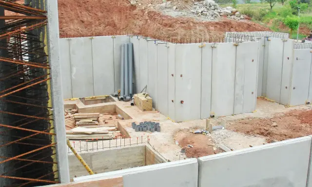 Construcción de un muro de contención con paneles prefabricados de hormigón. Se observan tuberías y materiales de construcción en el sitio.