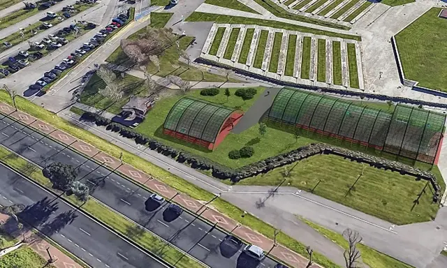 Vista aérea de un complejo deportivo con dos invernaderos verdes y una zona de aparcamiento. El **parque de las llamas** se extiende hasta la carretera.