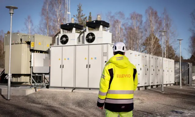 En person i gul jacka står framför en stor fristående batterilagring.