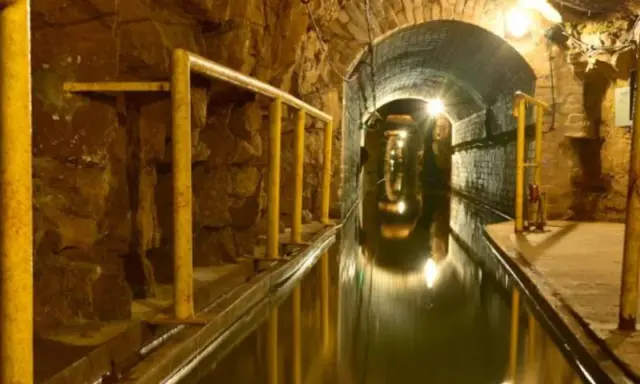 Podziemny tunel z wodą i żółtymi poręczami, idealny na zwiedzanie kopalni.