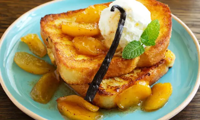 Délicieux pain perdu brioché, garni de fruits caramélisés, d'une boule de glace à la vanille et d'une gousse de vanille.