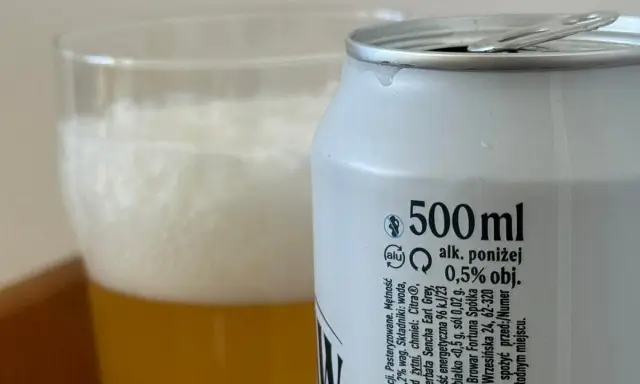Piwo z puszki z etykietą "alk. poniżej 0,5% obj." obok szklanki z pianką. Sprawdzamy, ile promili ma to piwo.