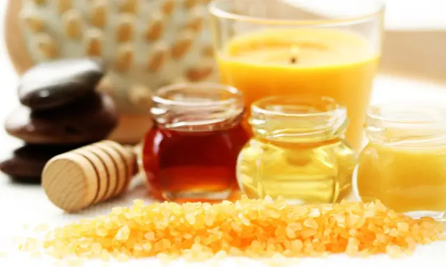 Ingredientes para un exfoliante corporal casero: sales, miel, aceites y una vela aromática.