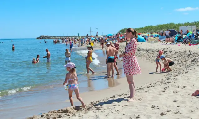 Słoneczne wczasy pod gruszą na plaży. Ludzie kąpią się w morzu i opalają na piasku. Dzieci bawią się w wodzie i budują zamki z piasku.