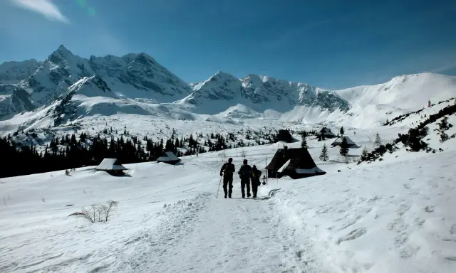 Trzej turyści idą szlakiem przez zasypane śniegiem Tatry. Widok idealny na tatry zimą dla średniozaawansowanych.