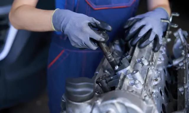 Mecánico con guantes trabajando en un motor, mostrando componentes como inyectores y partes del cigüeñal.