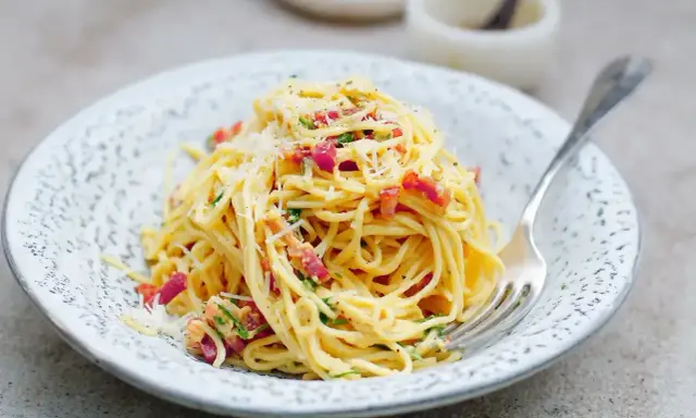 Pyszna carbonara ze śmietaną, okraszona boczkiem i parmezanem, czeka na widelcu.