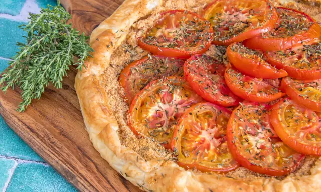 Une délicieuse tarte tomates aux herbes, sur une planche en bois, avec une branche de thym frais à côté.