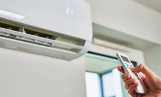 Mano con control remoto ajustando el aire acondicionado a 21 grados. ¿Es mejor apagar el aire acondicionado o dejarlo encendido?