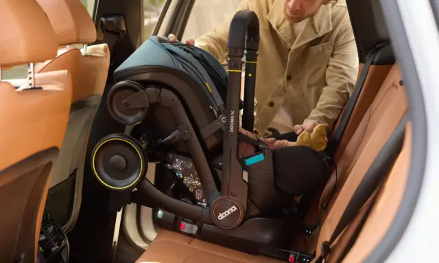 Mężczyzna wyjmuje fotelik z isofix z samochodu. Widać uchwyt i koła fotelika.