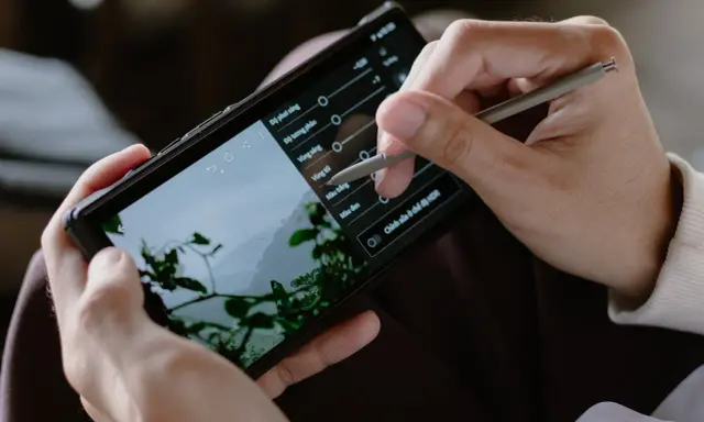 Ręce trzymają smartfon, na którym edytowany jest film. Stylus dostosowuje parametry, by pokazać, jak zrobić film na TikToku.