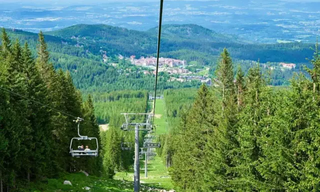 Kolejka linowa w Górach Izerskich, w kierunku najwyższego szczytu. Widok na las i zabudowania.