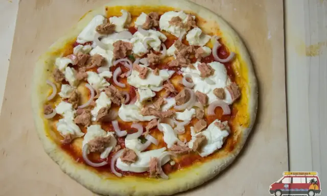 Gotowa do pieczenia pizza z tuńczykiem, mozzarellą i cebulą na drewnianej desce.