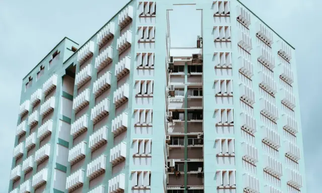 Edificio de apartamentos de color menta con filas de ventanas y persianas blancas. Un recordatorio de que se puede echar a un inquilino por necesitar el piso.