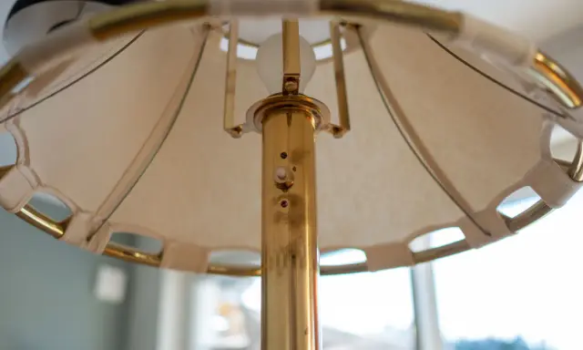 Detaljbild av en golvlampa i mässing från Ateljé Lyktan. Skärmen är av tyg med mässingsdetaljer.