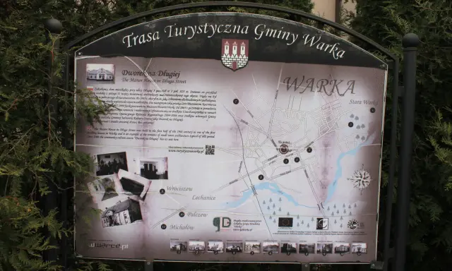 Mapa turystyczna gminy Warka z zaznaczonymi zabytkami, w tym Dworkiem na Długiej. W tle drzewa, a na dole strony logo "Warka" i adres strony.