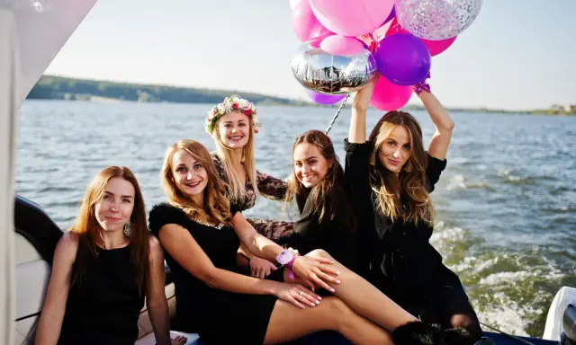 Uśmiechnięte kobiety na łodzi z balonami, celebrujące organizację wieczoru panieńskiego.