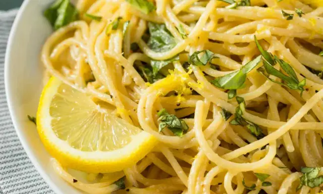 Spaghetti al limone cremosi, guarniti con scorza di limone e basilico fresco. Un piatto invitante e profumato.