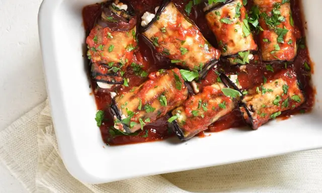 Involtini di melanzane ripieni di formaggio, cotti in sugo di pomodoro e guarniti con prezzemolo fresco.