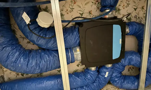 Système VMC installé dans un faux plafond. Les gaines bleues isolées sont connectées à une unité centrale noire. Un bon choix de VMC est essentiel pour la qualité de l'air intérieur.