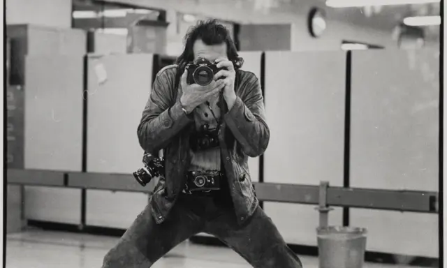 Un uomo con più macchine fotografiche al collo, intento a scattare un autoscatto. Un'immagine che cattura l'essenza di un fotografo, forse lo stesso René Burri.