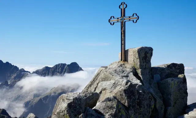 Krzyż na skalistym szczycie Gerlach. Widok na Tatry Wysokie ponad morzem chmur.