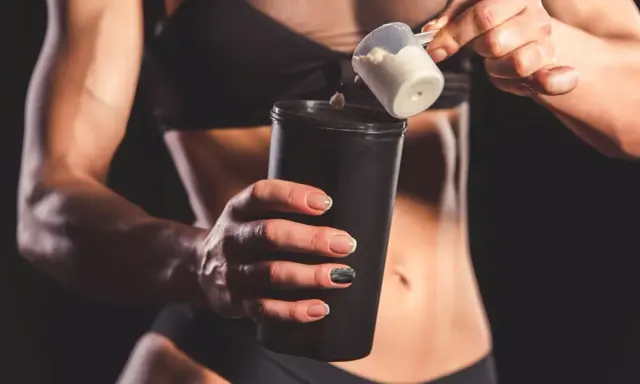 Kobieta z umięśnionym brzuchem dodaje proszek do shakera. Czy shake proteinowy jest zdrowy? To zależy od składu.