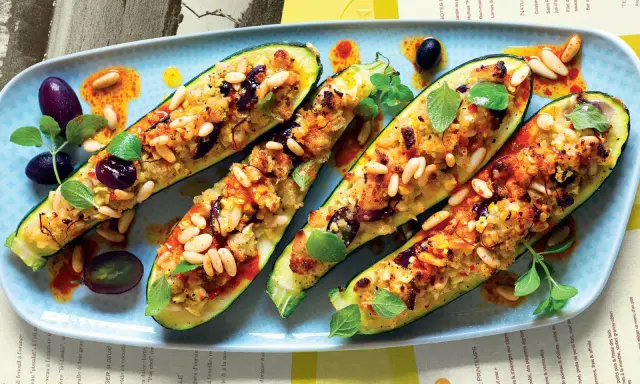 Zucchine ripiene vegetariane con pinoli, olive e erbe aromatiche, servite su un piatto azzurro con un filo d'olio piccante.