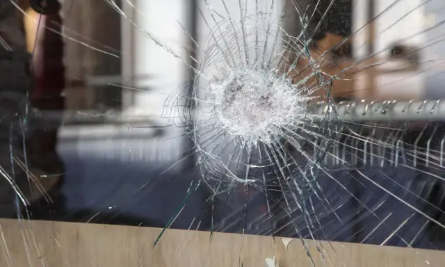 Une étoile de verre brisé se propage à travers la vitre, révélant un monde flou derrière.