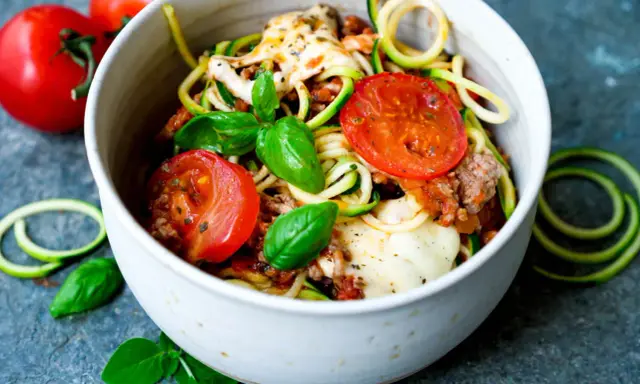 Herzhafte rezepte mit zucchini und hackfleisch: Zoodles mit Hackfleischsauce, Tomaten und geschmolzenem Käse, garniert mit frischem Basilikum.