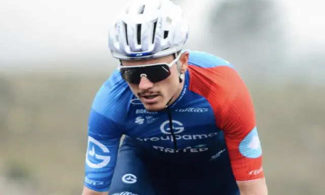 David Gaudu im blauen und roten Trikot, mit Helm und Sonnenbrille, konzentriert sich auf das Rennen.