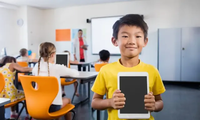 Un bambino sorridente in classe mostra un tablet, pronto per le attività di accoglienza di un nuovo alunno.