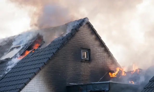 Un incendie maison ravage le toit, des flammes vives et une épaisse fumée s'échappent des tuiles.