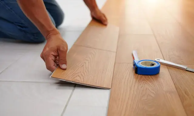 Pose d'un nouveau revêtement de sol imitation bois, une solution pour niveler un sol sans ragréage. Un mètre ruban et un cutter sont à proximité.