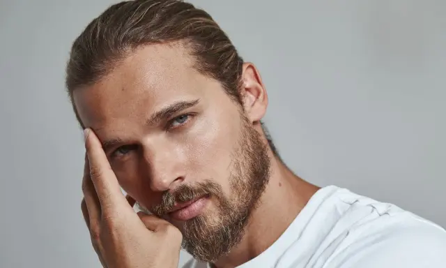 Un homme pensif, sa main effleurant son front, un sourcil plus haut que l'autre, regard intense.