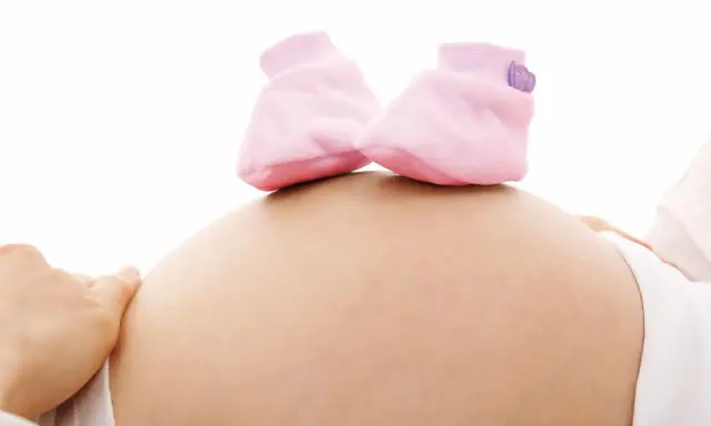 Close-up of a pregnant belly with tiny pink baby booties on top.