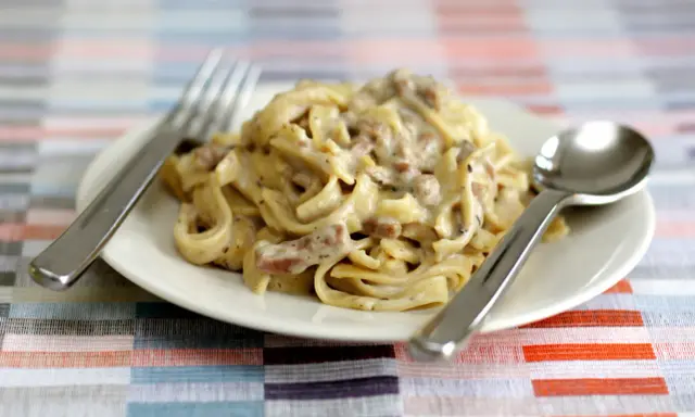 Un piatto di tagliatelle ai funghi cremose, pronte per essere gustate con forchetta e cucchiaio.