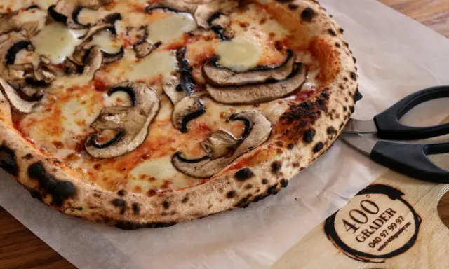 En nybakad champinjonpizza med bubblande ost, redo att skäras med saxen. En perfekt pizza för alla som gillar 400grader recensioner.