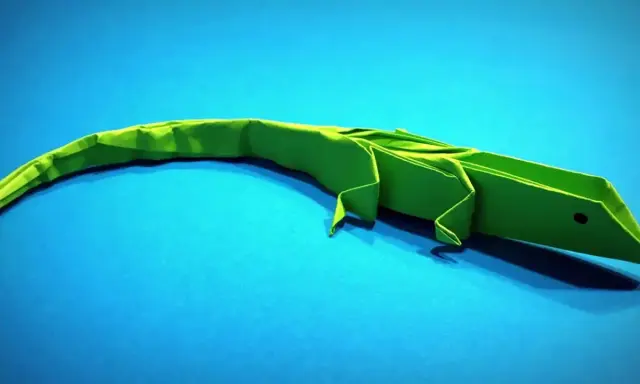 Un lagarto verde de papiroflexia animales descansa sobre un fondo azul.