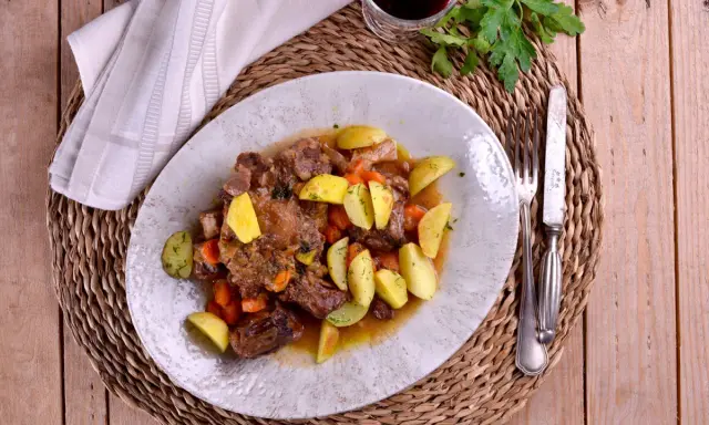 Plato de rabo de toro estofado con patatas y zanahorias, bañado en una salsa de vino blanco.