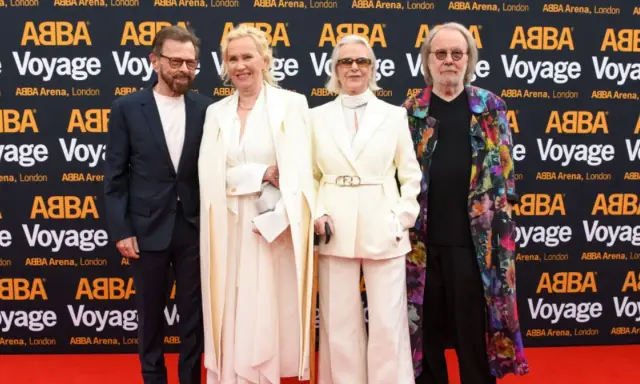 Członkowie zespołu ABBA na czerwonym dywanie, pozujący do zdjęć przed banerem "ABBA Voyage".