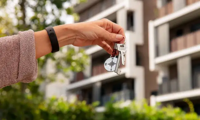 Mano con llaves y brújula, con un edificio moderno de fondo. Llevo 10 años de alquiler, me pueden echar.